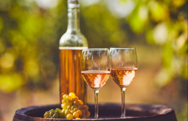 Bottiglia, due calici di vino macerato, vicini a un grappolo d’uva su una botte